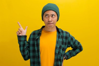 Heyecanlı genç Asyalı bir adam, bereli bir şapka ve gündelik bir gömlek giymiş, parmağını boş bir fotokopi alanını işaret ederek sarı bir arkaplan üzerinde duruyor.