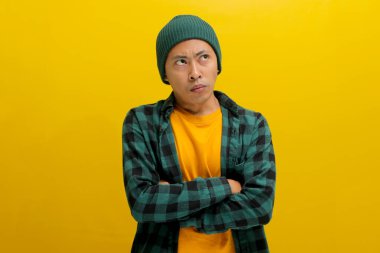 Kızgın, gücenmiş Asyalı genç bir adam kollarını kavuşturmuş, tatminsiz ya da hoşnutsuz bir tavır sergiliyor ve sarı arka planda izole edilmiş boş fotokopi alanına bakıyor..