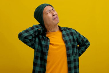 Asyalı adam boynuna masaj yapar ve sırtına dokunur. Aşırı çalışmanın yol açtığı kas ağrısını azaltır. Sarı arka planda izole olur..