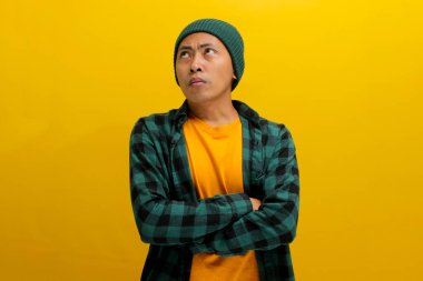 Kızgın, gücenmiş Asyalı genç bir adam kollarını kavuşturmuş, tatminsiz ya da hoşnutsuz bir tavır sergiliyor ve sarı arka planda izole edilmiş boş fotokopi alanına bakıyor..