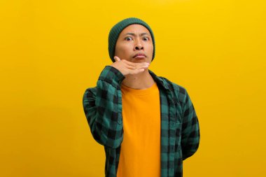 Asyalı rahatsız bir genç adam, bereli şapka ve gündelik gömlek giymiş, İtalyan el hareketi yapıyor. Sarı arka planda dururken kayıtsızlık ya da umursamazlığı simgeliyor.