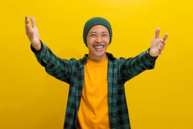 Aşırı neşeli Asyalı bir adam, bereli bir şapka ve gündelik bir gömlek giyer, kollarını kameraya doğru açar, bir sarılma jesti sunar, sarı bir arka planda dururken bir kucaklaşmayı davet eder