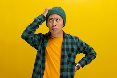 Kafası karışmış genç Asyalı bir adam, bereli bir şapka ve gündelik bir gömlek giymiş, bir anlık tefekkür ile tasvir ediliyor, başını kaşıyor, sarı arka planda dururken bir çözüm üzerinde kafa yoruyor..