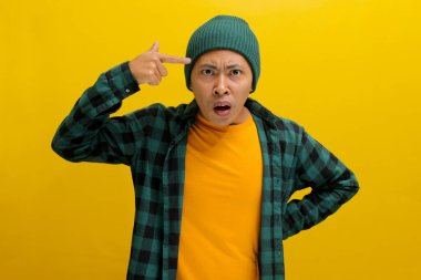 Şapkalı ve sıradan gömlekli kızgın genç Asyalı adam parmağını şakağına dayayıp işaret ediyor ve görünüşe göre 