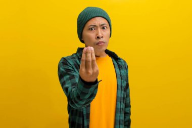 Şapkalı ve rahat gömlekli genç bir Asyalı, sarı arka planda dururken tipik bir İtalyan el hareketi yapıyor..