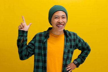 Heyecanlı genç Asyalı bir adam, bereli bir şapka ve gündelik bir gömlek giymiş, parmağını boş bir fotokopi alanını işaret ederek sarı bir arkaplan üzerinde duruyor.