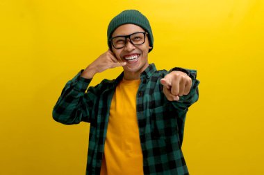 Hevesli Asyalı genç bir adam, bereli bir şapka ve sıradan bir gömlek giyer, enerjik bir şekilde kameraya doğru bakarken sarı arka planda dikilirken beni arar..