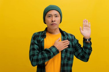 Şapka ve günlük gömlek giyen genç Asyalı bir adam, elini göğsüne koyar parmaklarını kaldırır, yemin eder ya da söz verir, sadakat ve bağlılığı vurgular, sarı fon