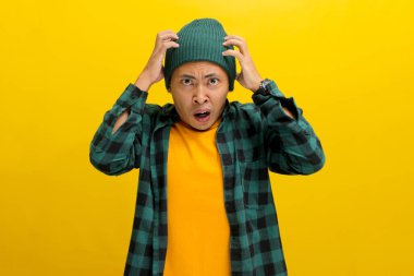 Şok olmuş ve endişeli Asyalı genç bir adam paniklemiş görünüyor, ellerini başının üstüne koyup korkmuş bir ifadeyle kameraya bakıyor, bir başarısızlık duygusuyla korkmuş ve bunalmış hissediyor.