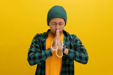 Şapka ve gündelik gömlek giymiş genç bir Asyalı ellerini dua etmek için tokalaşıyor, zarafet, umut, af diliyor, dini bir kavramı somutlaştırıyor. Sarı arkaplanda izole edilmiş