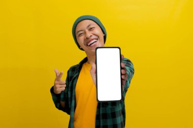 Heyecanlı Asyalı bir adam, bereli bir şapka ve günlük bir gömlek giymiş, boş beyaz ekranlı bir cep telefonuna bakıyor, yeni bir uygulama veya özel bir teklif öneriyor ya da öneriyor.