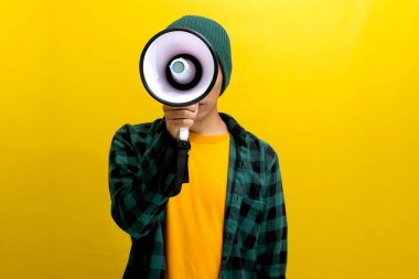 Şapkalı Asyalı aktivist megafona bağırıyor ve insan hakları ve adaleti protesto etmek için konuşma özgürlüğü için bağırıyor. Sarı arka planda izole edilmiş.