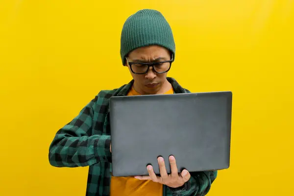 stock image A young Asian freelance worker appears puzzled and lost in thought as he gazes at his laptop while working remotely from home. Engrossed in reading an email from a client, long hours of work concept