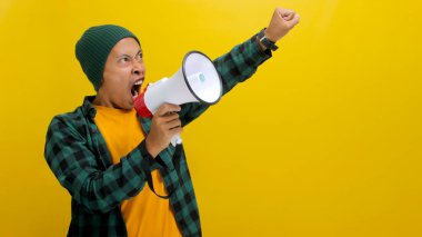 Asian man activist in a beanie hat shouts and yells into a megaphone, demanding change and protesting for human rights or justice with a focus on freedom of speech. Isolated on a yellow background clipart