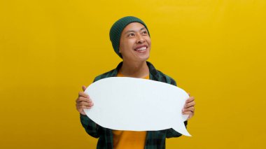 Heyecanlı Asyalı bir adam, bereli bir şapka ve gündelik bir gömlek giymiş, sarı bir zemin üzerinde dururken, bir konuşma baloncuğunu tutuyor ve ona bakıyor.