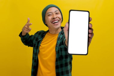 Heyecanlı Asyalı bir adam, bereli bir şapka ve günlük bir gömlek giymiş, boş beyaz ekranlı bir cep telefonuna bakıyor, yeni bir uygulama veya özel bir teklif öneriyor ya da öneriyor.