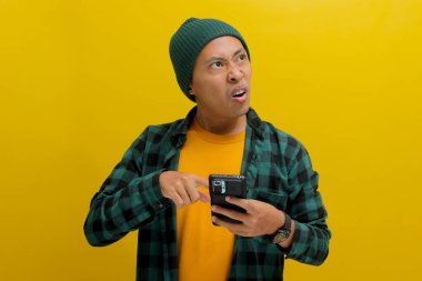 Şaşkın Asyalı bir adam, bereli bir şapka ve gündelik bir gömlek giyer, telefonunda sarı bir arka plana karşı durarak özel bir indirime şaşırır.