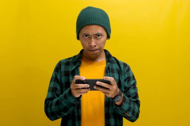 Sıkılmış Asyalı bir adam, bereli bir şapka ve sıradan bir gömlek giyiyor, sıkıcı bir video izlerken ya da telefonuyla sıkıcı bir oyun oynarken sarı arka planda dikilirken sıkılmış görünüyor.