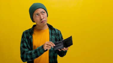 Tereddütlü bir Asyalı genç adam, elinde para dolu bir cüzdan tutarken kazancını artırmak için stratejiler düşünüyor. Fonu akıllıca mı yatırmalı yoksa başka bir yere mi ayırmalı diye düşünüyor.