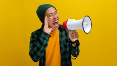 Bereli ve rahat gömlekli heyecanlı Asyalı adam, haberleri, özel bir teklifi, indirimi veya satışı paylaşmak için hoparlörü kullanarak megafonla bir duyuru yapıyor. Sarı arka planda izole edilmiş..