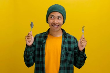 Aç Asyalı bir adam, bereli bir şapka ve günlük bir gömlek giyer, çatal ve kaşıkla dudaklarını ısırır, yaramaz bir ifadeyle kameraya bakar, yoğun açlığını gösterir.