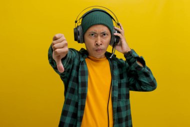 Bere takmış Asyalı bir adam kulaklıkla müzik dinlerken tasvip etmediği için kaşlarını çatıyor. Müzikten hoşlanmıyormuş gibi davranarak el hareketi yapıyor. Sarı arka planda izole edilmiş..