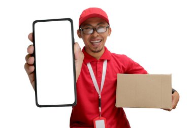 Asyalı kurye ya da kurye kameraya beyaz arka planda izole edilmiş karton bir paket tutarken boş beyaz ekran ekranlı bir telefon gösteriyor.