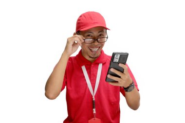 Heyecanlı Asyalı kurye ya da kurye gözlüğünü ayarlıyor, elinde telefon tutarken kameraya bakıyor. Beyaz bir arkaplanda izole edilmiş