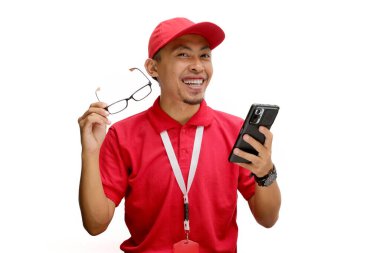 Heyecanlı Asyalı kurye ya da kurye gözlüğünü ayarlıyor, elinde telefon tutarken kameraya bakıyor. Beyaz bir arkaplanda izole edilmiş