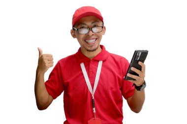 Gözlüklü Asyalı teslimatçı elinde akıllı telefon tutuyor, yeni uygulamalar tavsiye ediyor, olumlu yorumlar yapıyor ya da geri bildirim yapıyor. Kameraya baş parmak işareti yapıyor, beyaz bir arkaplanda izole edilmiş.