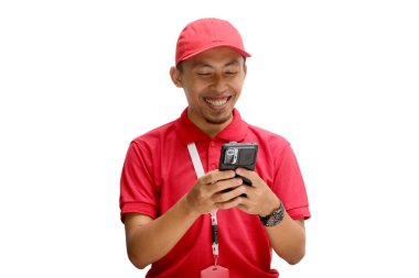 Kırmızı şapkalı ve kırmızı polo tişörtlü neşeli bir Asyalı kurye. Telefonuna mesaj atıyor. Başarılı bir alışveriş ya da teslimat hakkında iyi haberler alıyor. Beyaz bir arkaplanda izole edilmiş