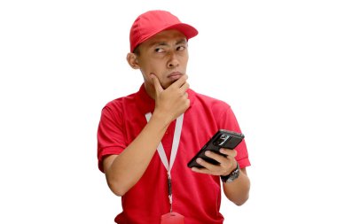 Düşünceli bir Asyalı kurye ya da kurye düşünceli bir jest yapıyor, elinde telefon tutarken bir şeyler düşünüyor. Beyaz bir arkaplanda izole edilmiş