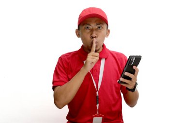 Asyalı teslimatçı, parmaklarını dudaklarının üzerine koyarak, bir telefon tutarken sınırlı bir teklif ya da indirimle ilgili bir sırrı saklaması için işaret veriyor. Beyaz bir arkaplanda izole edilmiş.