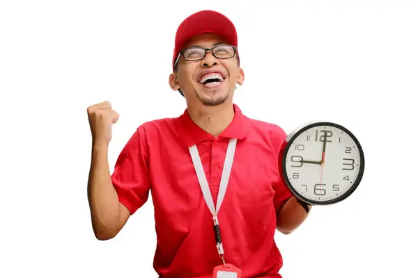 stock image Excited Asian delivery man or courier clenches his fist in a YES gesture while holding a clock in his hand, celebrating success in on-time express delivery. Isolated on a white background