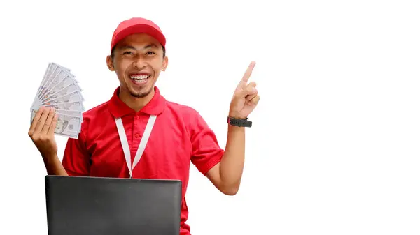 stock image Asian delivery man, holding money while using a laptop against a white background. Concept of professionalism, e-commerce management, financial transactions, delivery services, and business efficiency