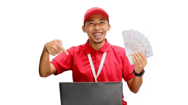 stock image Asian delivery man, holding money while using a laptop against a white background. Concept of professionalism, e-commerce management, financial transactions, delivery services, and business efficiency