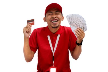 Kırmızı polo tişört giyen Asyalı teslimatçı beyaz arka planda kredi kartı ve dolar banknotları tutuyor. Teslimat hizmetleri, finansal işlemler, e-ticaret ve müşteri memnuniyeti.
