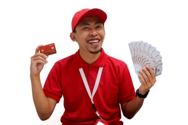 Kırmızı polo tişört giyen Asyalı teslimatçı beyaz arka planda kredi kartı ve dolar banknotları tutuyor. Teslimat hizmetleri, finansal işlemler, e-ticaret ve müşteri memnuniyeti.
