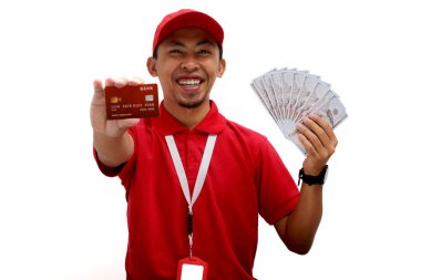 Kırmızı polo tişört giyen Asyalı teslimatçı beyaz arka planda kredi kartı ve dolar banknotları tutuyor. Teslimat hizmetleri, finansal işlemler, e-ticaret ve müşteri memnuniyeti.