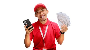Asyalı teslimatçı elinde telefon ve para banknotları tutarken kameraya gülümsüyor. Teslimat hizmetleri, e-ticaret işlemleri ve dost canlısı müşteri hizmetleri kavramları