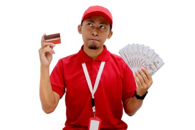 Düşünceli Asyalı teslimatçı derin düşüncelere dalmışken kredi kartı ve dolar banknotları tutuyor. Mali kararlar, e-ticaret, dağıtım hizmetleri, harcamalar ve yatırımlar kavramı.