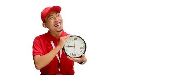 stock image Excited Asian delivery man or courier holds a clock with joyful expression, isolated on white background. Concept of time management, speedy service, reliable delivery, logistics and courier services