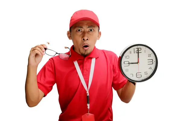 stock image Asian delivery man or courier looks surprised as he points at a clock in his hand, isolated on a white background. Concept of unexpected deadlines, urgent deliveries, logistics and delivery services