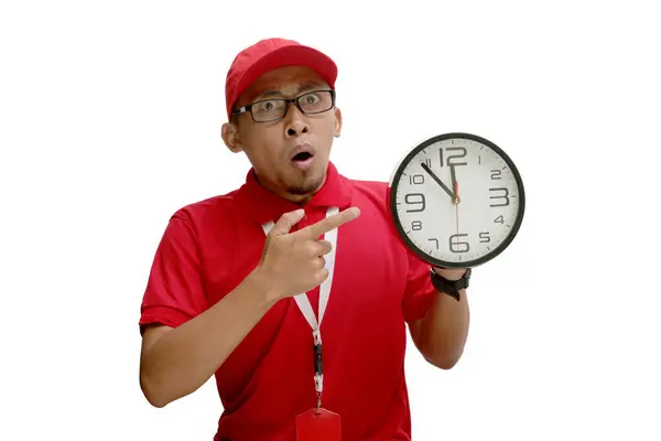 stock image Asian delivery man or courier looks surprised as he points at a clock in his hand, isolated on a white background. Concept of unexpected deadlines, urgent deliveries, logistics and delivery services