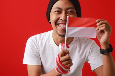 Endonezya bayrağını taşıyan heyecanlı Endonezyalı genç adam, 17 Ağustos 'ta Endonezya Bağımsızlık Günü' nü kırmızı arka planda kutluyor.