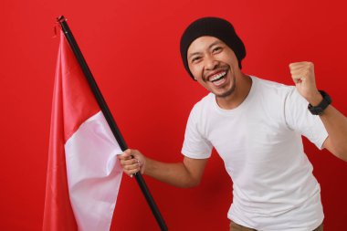 Heyecanlı Endonezyalı genç adam Endonezya bayrağını kaldırarak 17 Ağustos 'taki Bağımsızlık Günü' nü kutluyor. Olay yeri kırmızı bir arkaplanda izole edilmiş.