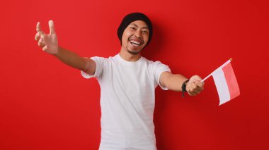 Endonezyalı adam, Endonezya bayrağıyla kameraya sarılmak için kollarını açıyor ve 17 Ağustos 'taki Endonezya Bağımsızlık Günü kutlamalarına katılması için birini davet ediyor.