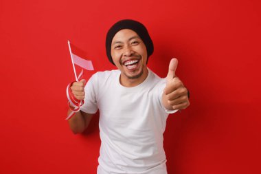 Endonezya gençliği, 17 Ağustos 'ta Endonezya Bağımsızlık Günü' nü kutlarken ve kırmızı zemin üzerinde izole edilmiş Endonezya bayrağını tutarken kameraya olumlu bir hareket gösteriyor.