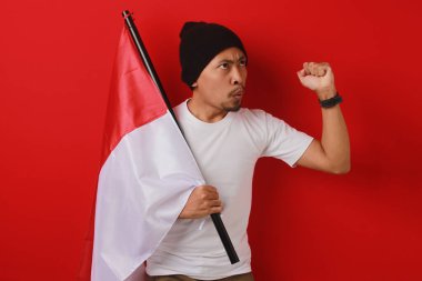 Endonezyalı genç adam 17 Ağustos 'ta Endonezya' nın Bağımsızlık Günü kutlamalarında elinde bir Endonezya bayrağı tutarken ve yumruğunu kaldırırken konuşma yapıyor. Sahne kırmızı arka planda izole edilmiştir..