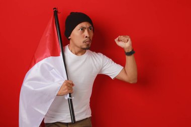 Endonezyalı genç adam 17 Ağustos 'ta Endonezya' nın Bağımsızlık Günü kutlamalarında elinde bir Endonezya bayrağı tutarken ve yumruğunu kaldırırken konuşma yapıyor. Sahne kırmızı arka planda izole edilmiştir..